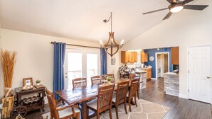 A spacious dining area with a wooden table and chairs, a chandelier, and a view into the kitchen.