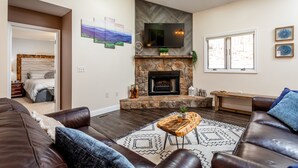 A living room with a stone fireplace, a flat-screen TV, and a large window.