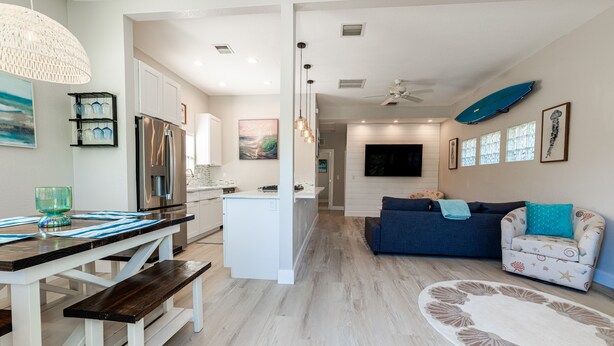 A modern kitchen with white cabinets, a stainless steel refrigerator, and a dining area with a wooden bench and a glass bowl.