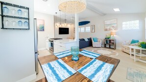 A modern living room with a wooden dining table, blue patterned placemats, a hanging light fixture, and a sofa.