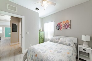 Ein Schlafzimmer mit Bett, Nachttisch, Deckenventilator, Kommode und Bildern an der Wand.