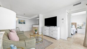 A modern living room with a sofa, coffee table, TV, and a dining area with chairs and a table. - Stylish Oceanfront Condo - Huge Balcony - 3 Pools, Lazy River, and Hot Tub (Myrtle Beach)