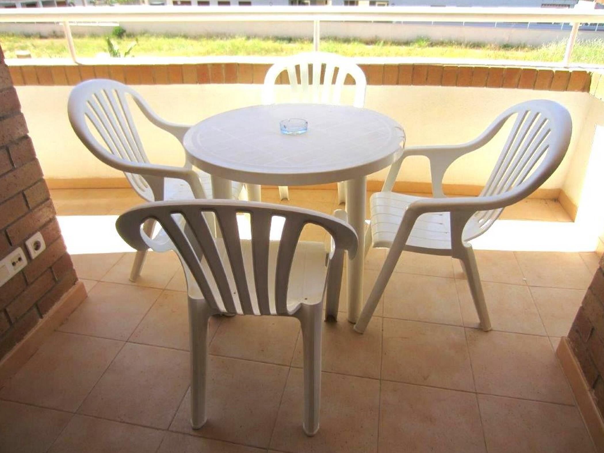Um pátio com uma mesa redonda e quatro cadeiras de plástico branco.