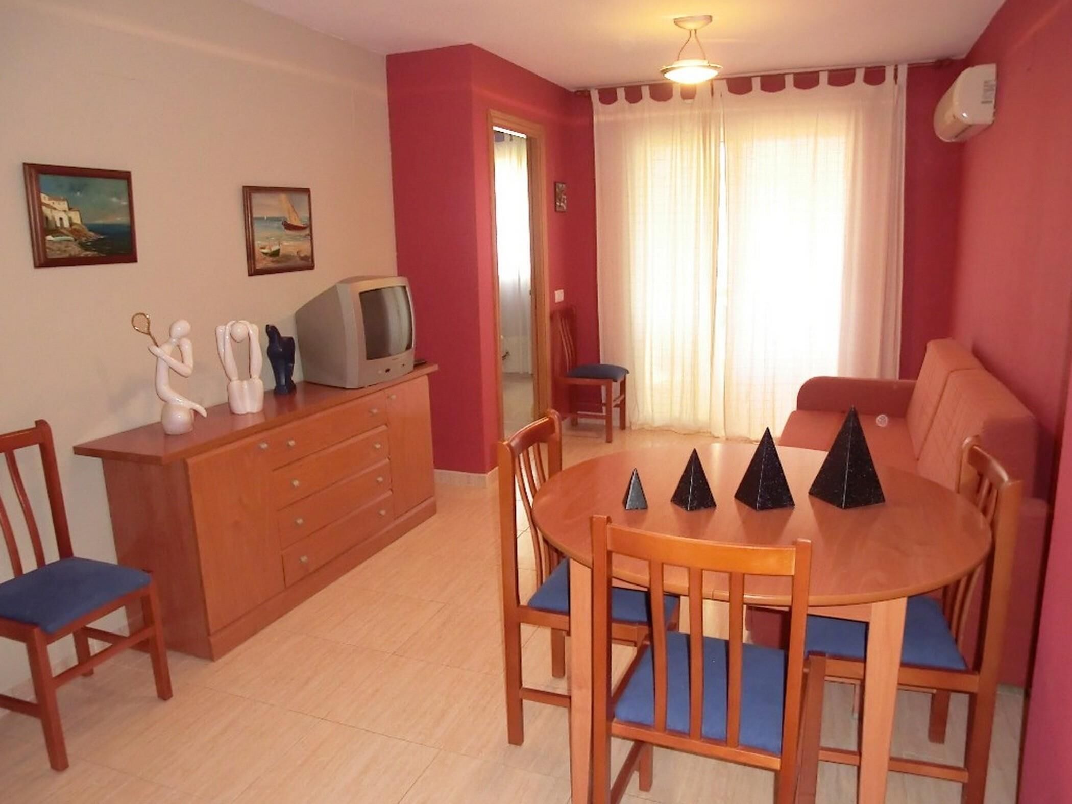 Un comedor con una mesa y sillas de madera, un televisor en un mueble y dos cuadros en la pared.