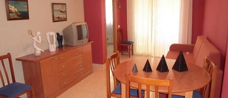 Un comedor con una mesa y sillas de madera, un televisor en un mueble y dos cuadros en la pared.