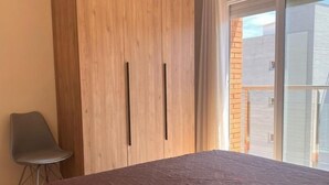 Ein Schlafzimmer mit einem Bett, einem Holzschrank, einem Stuhl und einer Glastür zum Außenbereich.