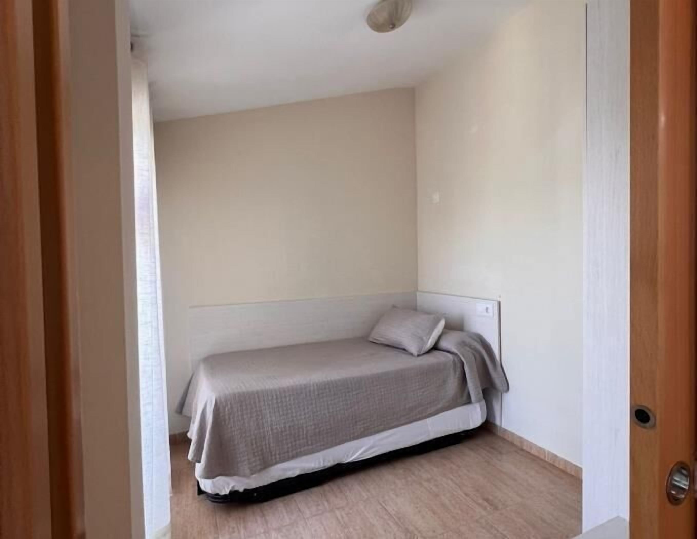 A small, single-bed room with a wooden floor and a plain white wall.