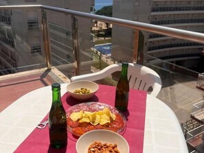 Ein Tisch mit Snacks, zwei Flaschen und einer Schüssel auf einem Balkon mit Geländer und Gebäuden im Hintergrund.