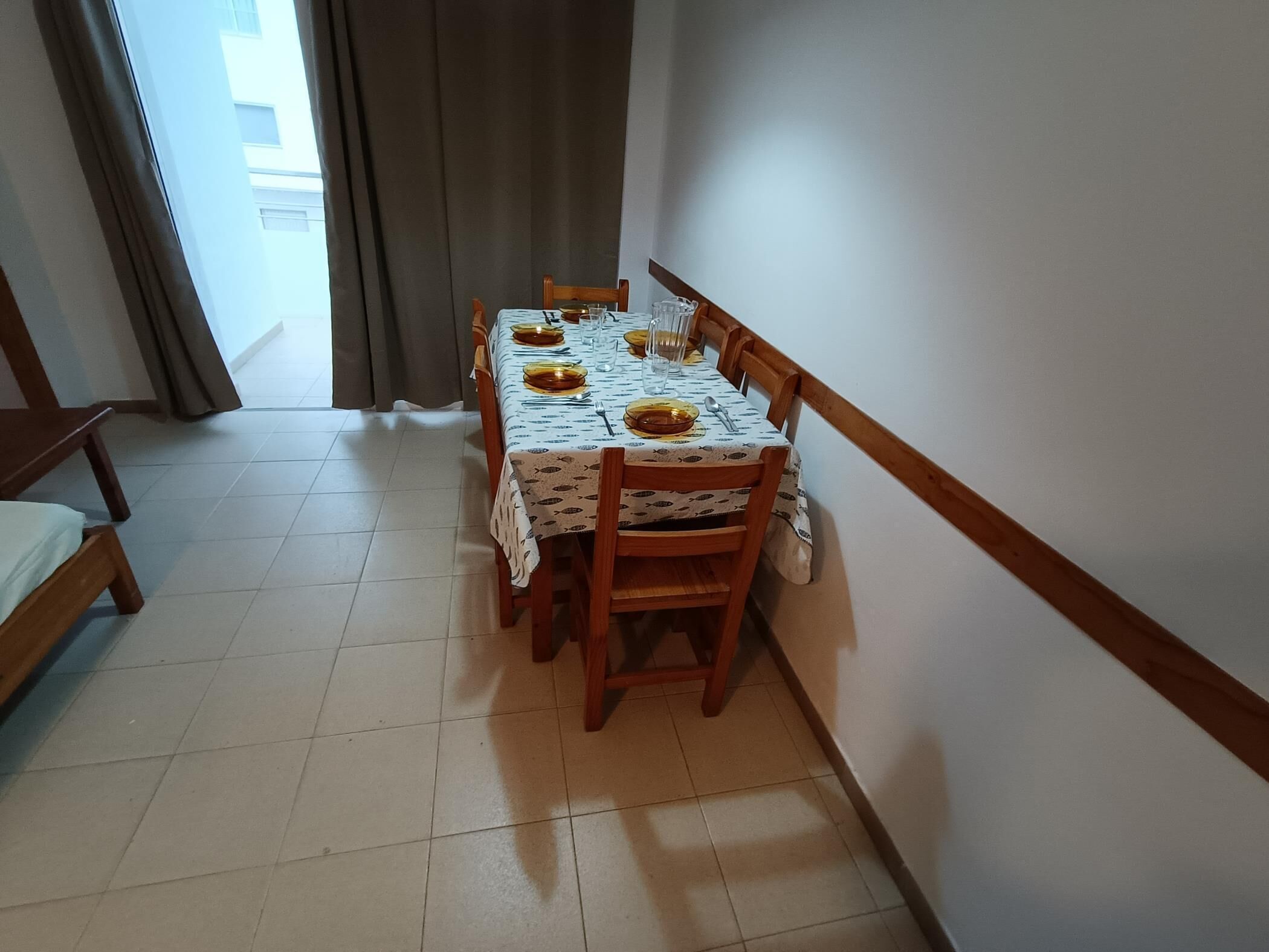 Comedor con mesa dispuesta para seis personas, sillas de madera y un banco.