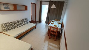 Una habitación compacta con sofá, una mesa de comedor preparada para cuatro personas y una cama individual.