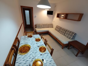 A dining area with a table set for four, a sofa, and a television mounted on the wall.
