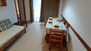 Una habitación pequeña con cama, una mesa de comedor lista para cuatro personas y una ventana con cortinas.