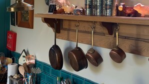 A kitchen with wooden shelves holding pots and pans, a hanging pot rack, and a window with a view of trees. - Shepherds Hut with Scandinavian Hot Tub and hydromassager  (Sway)