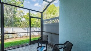 Un patio techado con vistas a un jardín césped y árboles. Hay dos sillas y una pequeña mesa.