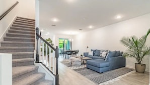 Una sala de estar moderna con una escalera alfombrada de color gris, un conjunto de sofá azul y un comedor con mesa y sillas.