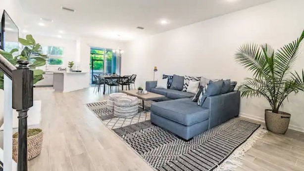 Una sala de estar moderna con un sofá azul, un comedor con mesa y sillas, y una cocina con encimera y armarios.