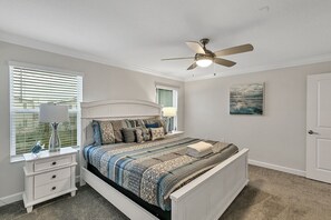 Un dormitorio con cama, mesita de noche, lámpara, ventilador de techo y un cuadro en la pared.
