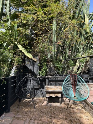 Relax in this serene outdoor seating area with two comfortable chairs and a wooden table, surrounded by lush greenery.