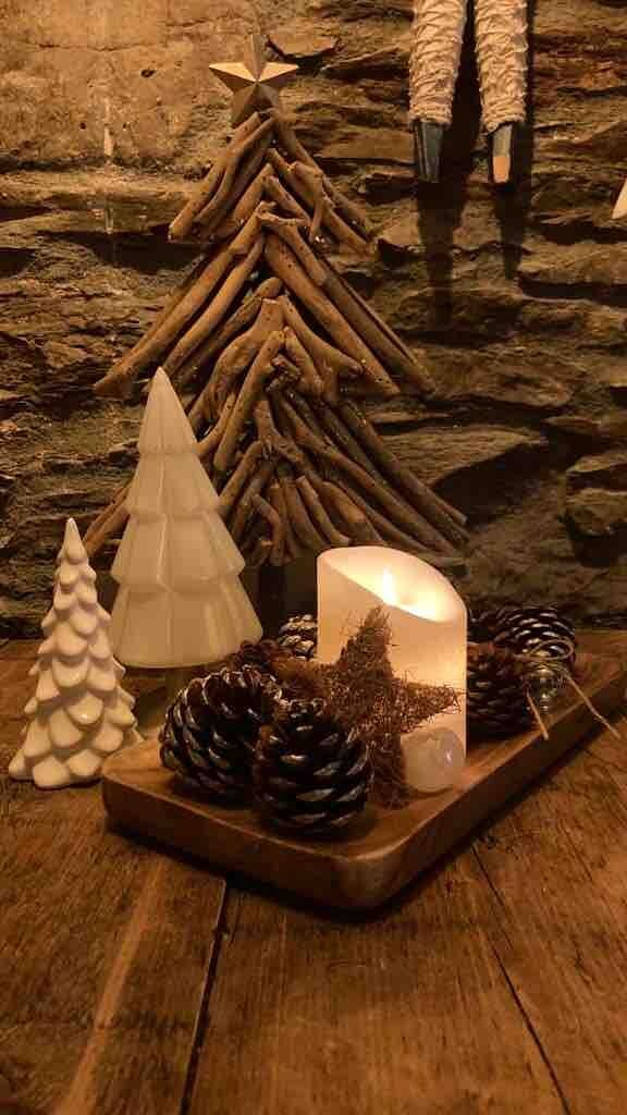 A rustic wooden table with a candle, pine cones, and a small white Christmas tree.