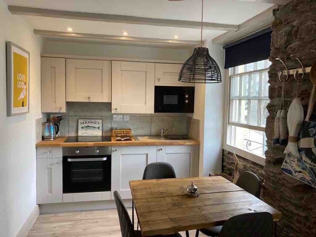 A modern kitchen with white cabinets, a black oven, and a wooden dining table.