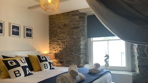 Een slaapkamer met een stenen muur, een bed met opgerolde handdoeken en een raam met gordijnen.