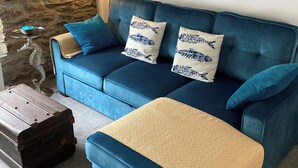 Una sala de estar con un sofá azul, un cuadro de un barco, una lámpara y una escultura de metal decorativa.