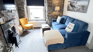Een gezellige woonkamer met een stenen muur, een blauwe bank, een gele fauteuil, een televisie en een open haard.