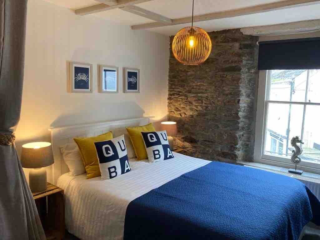 A bedroom with a bed, a stone wall, a window with a curtain, and a hanging light fixture.