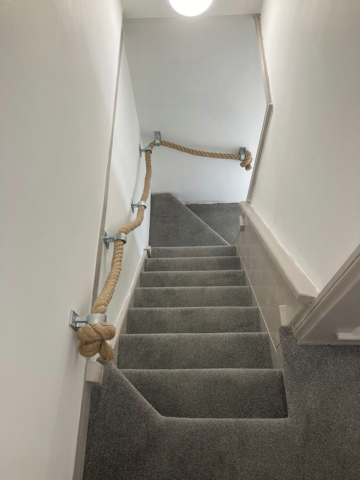 Una escalera con alfombra, barandilla de cuerda y soportes metálicos.