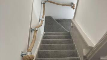 Una escalera con alfombra, barandilla de cuerda y soportes metálicos.