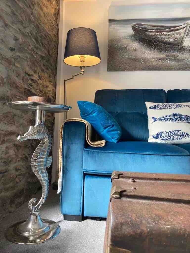 Une pièce avec un canapé bleu, une lampe en forme d’hippocampe, une lampe avec un abat-jour noir et un tableau représentant un bateau accroché au mur.
