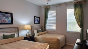 A hotel room with two beds, a desk, a ceiling fan, and two windows with curtains.