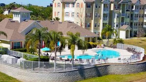 A multi-story residential building with a swimming pool surrounded by palm trees and lounge chairs.