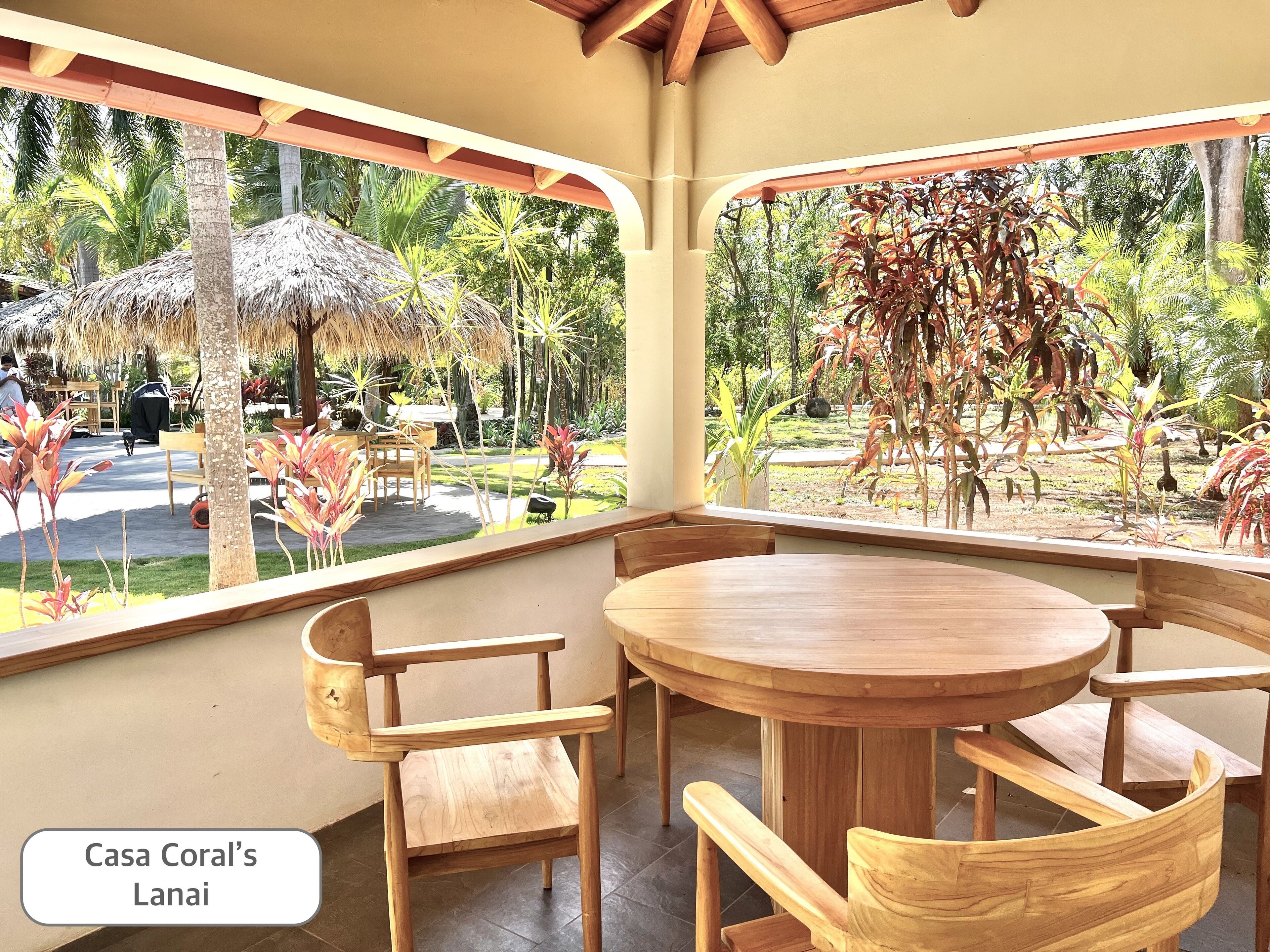 Un espace extérieur abrité, aménagé avec du mobilier en bois et offrant une vue sur un jardin tropical.