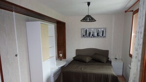 Een slaapkamer met een bed, nachtkastje, dressoir, spiegel en plafondventilator.