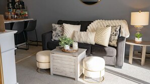 Ein Wohnzimmer mit grauem Sofa, einer Kaffeestation, einem runden Spiegel und einer Lampe.