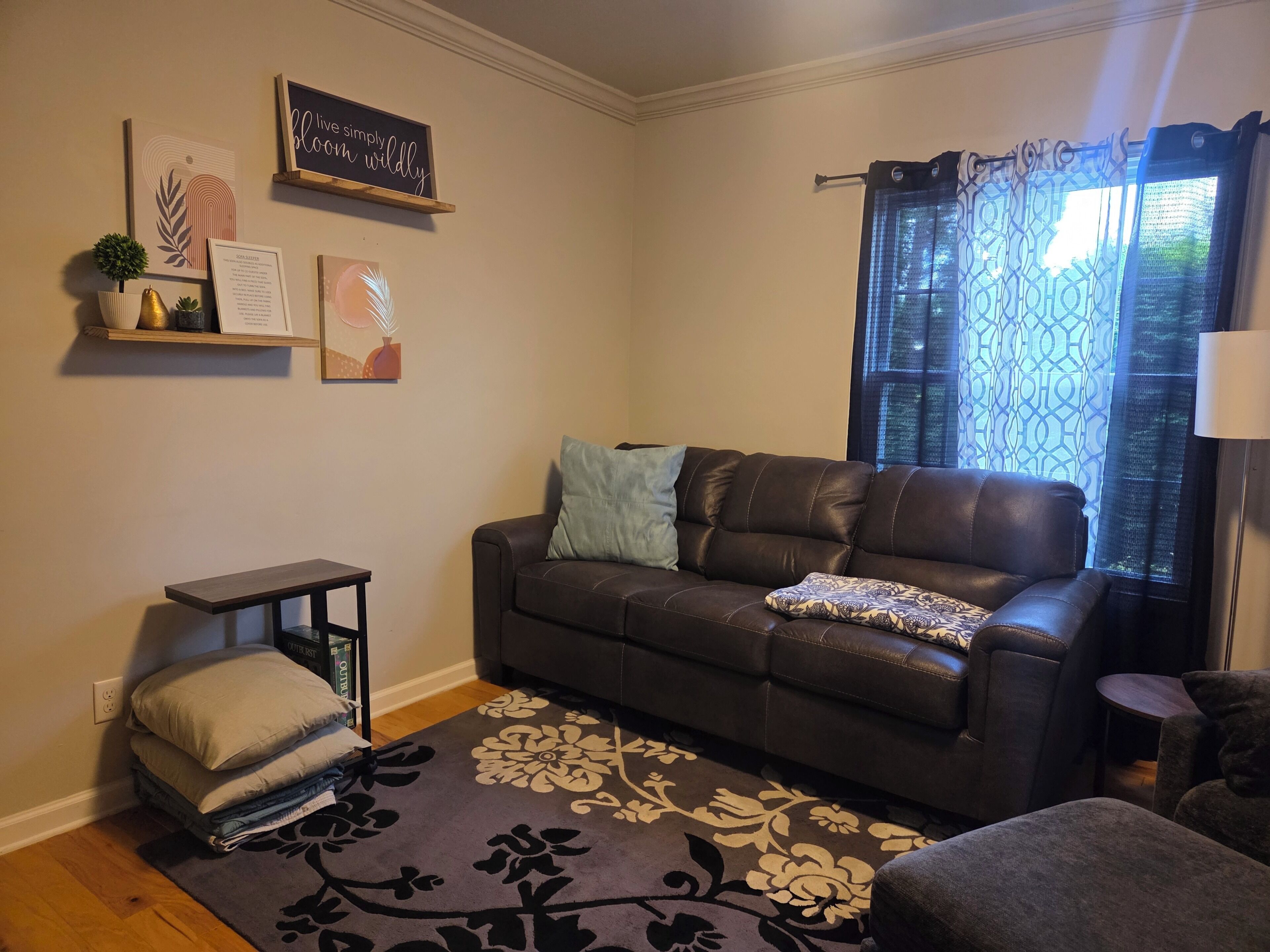 A living room with a brown leather sofa, a patterned rug, and a window with patterned curtains.