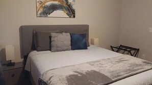 A bedroom with a bed, two bedside lamps, a headboard, and a painting on the wall.