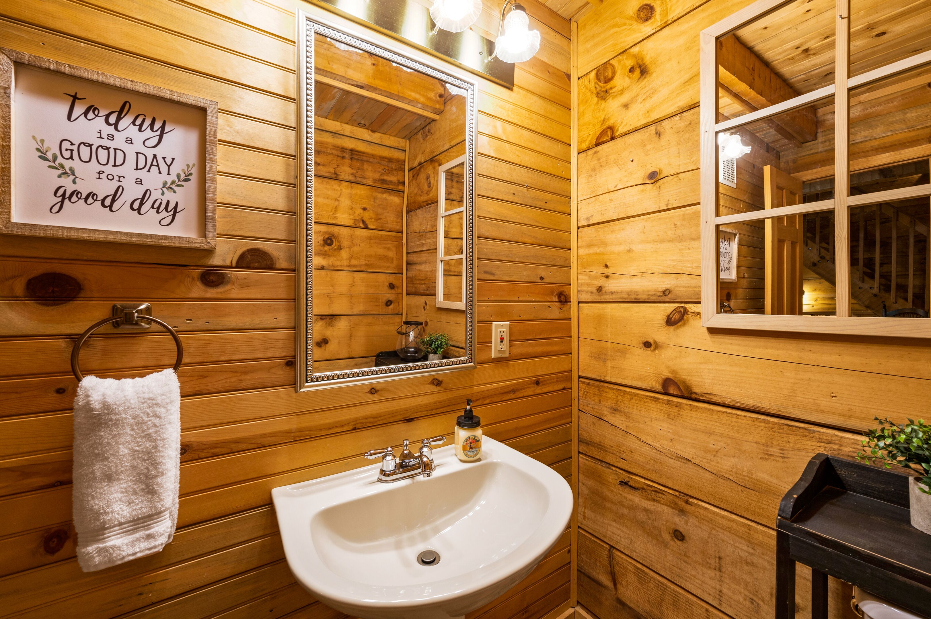 A wooden cabin bathroom with a white sink, a mirror, and a towel rack.