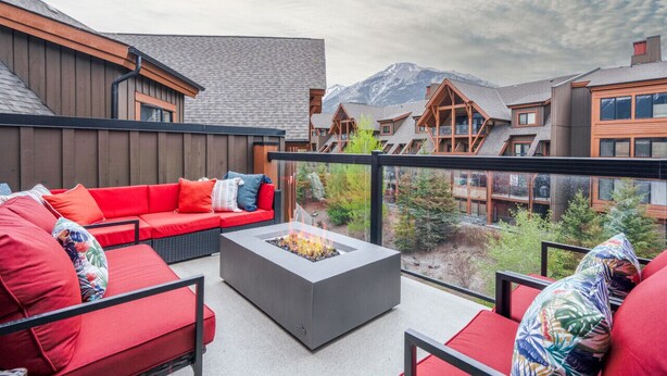 Un espace extérieur moderne aménagé avec des sièges, un foyer, du mobilier rouge et une vue sur les bâtiments situés en montagne.