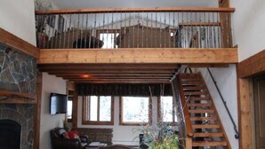 Een ruime woonkamer met een stenen open haard, een leren bank en een houten trap naar een hoger gelegen verdieping.