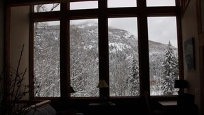 Een kamer met een groot raam dat uitkijkt op een besneeerd berglandschap.
