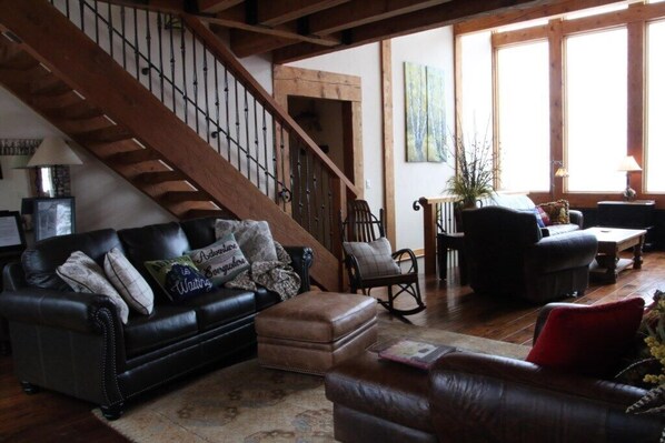 A spacious living room with a black leather sofa, a wooden rocking chair, and a wooden staircase.