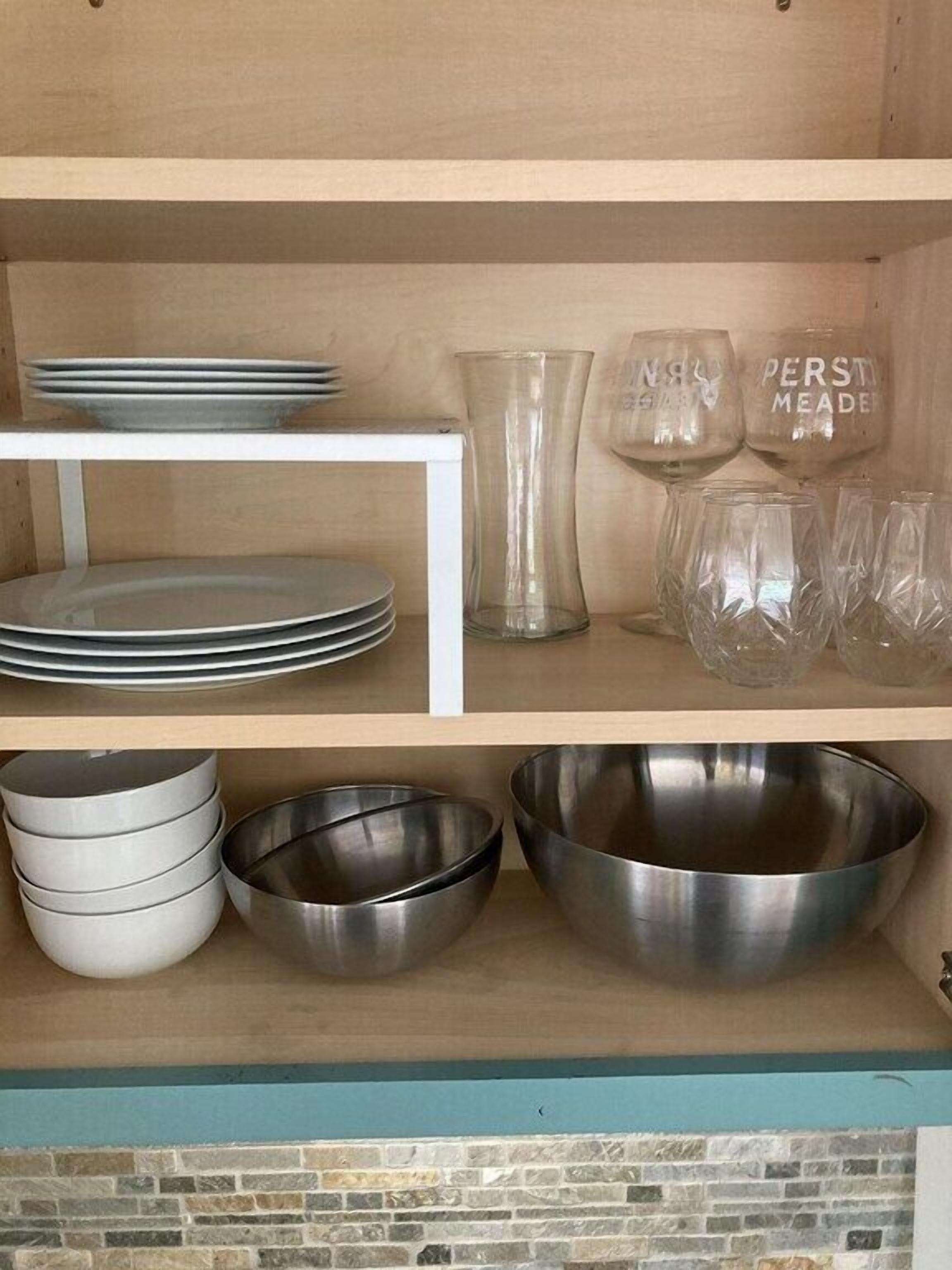 Une étagère de cuisine avec des assiettes empilées, un grand vase en verre et plusieurs verres à vin.