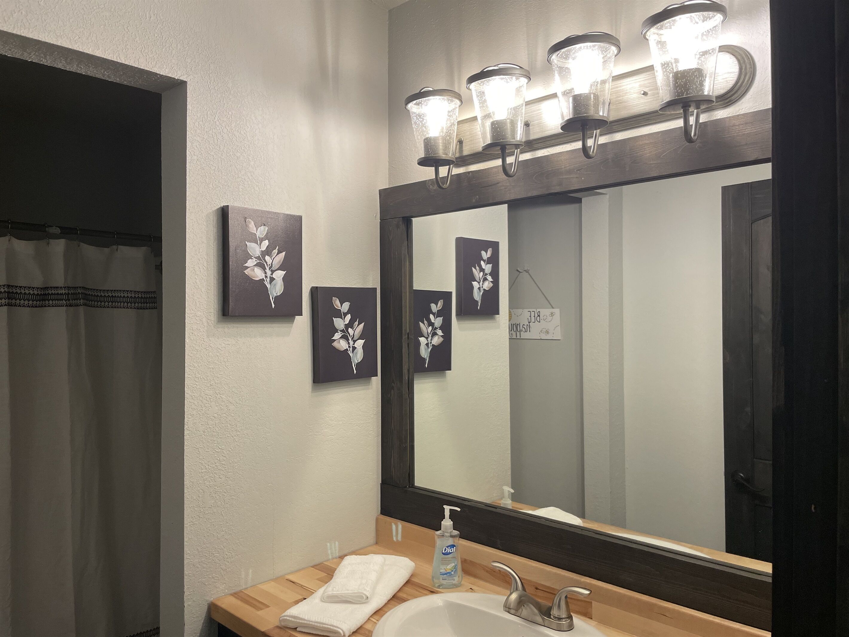 Casa de banho com um espelho grande, uma pia, uma toalha e três luminárias fixadas na parede.