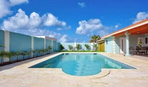 Una piscina con solárium de baldosas, palmeras y un edificio de techo rojo.