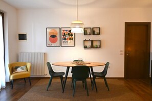 A dining area with a round table, four chairs, a pendant light, and framed artwork on the wall. - S255 - Sirolo, new three-room apartment a stone's throw from the center (Sirolo)