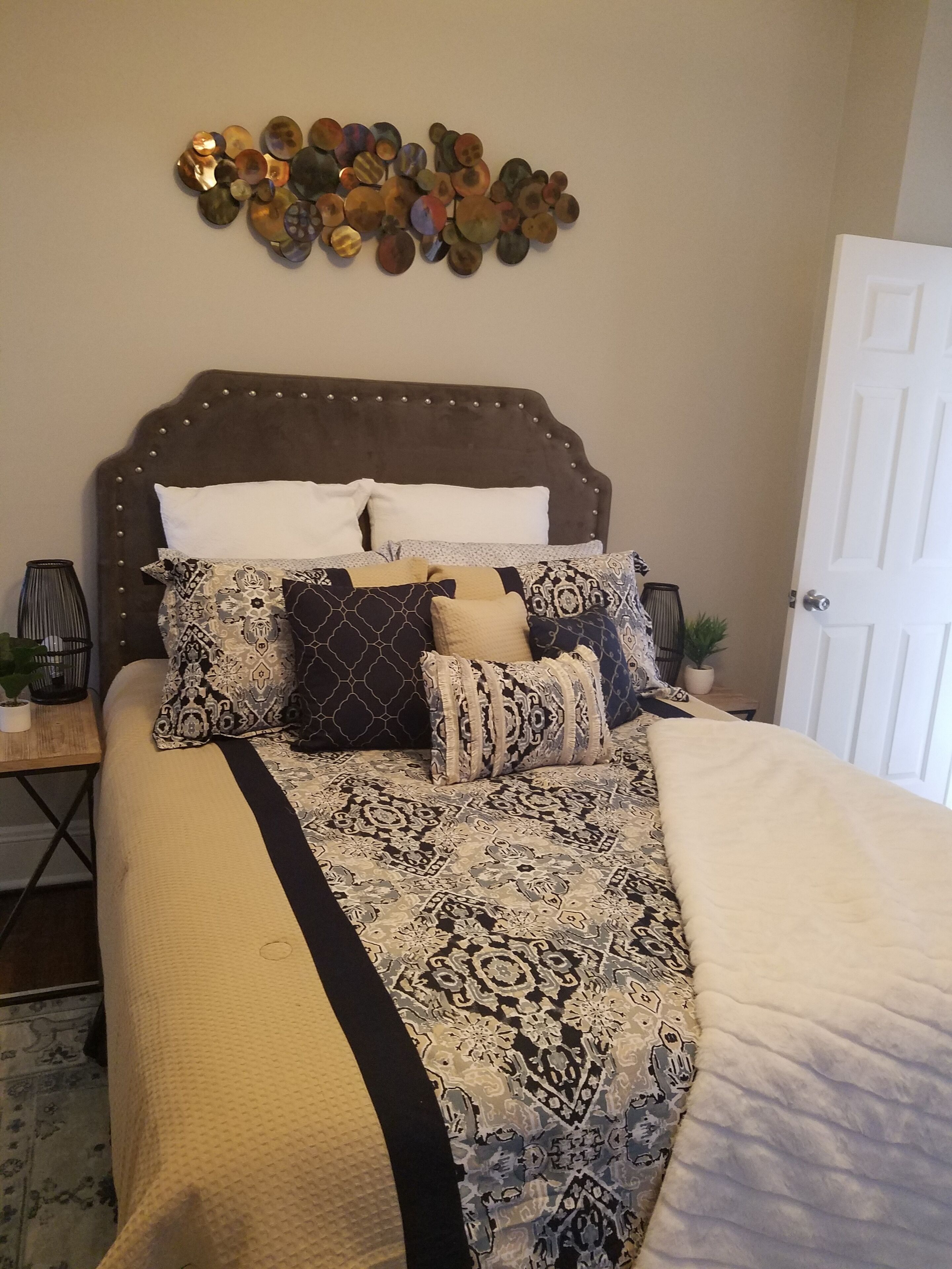 A bed with patterned bedding, a decorative wall piece above it, and a white door to the right.