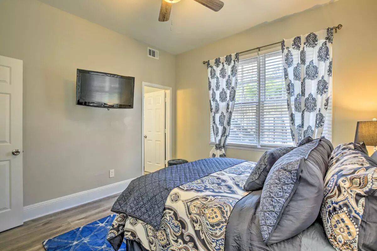 A bedroom with a bed, a TV mounted on the wall, and a window with patterned curtains.