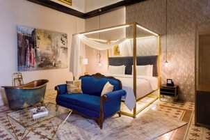 Una cama con dosel, un sofá azul, una mesa de centro de vidrio y una bañera.